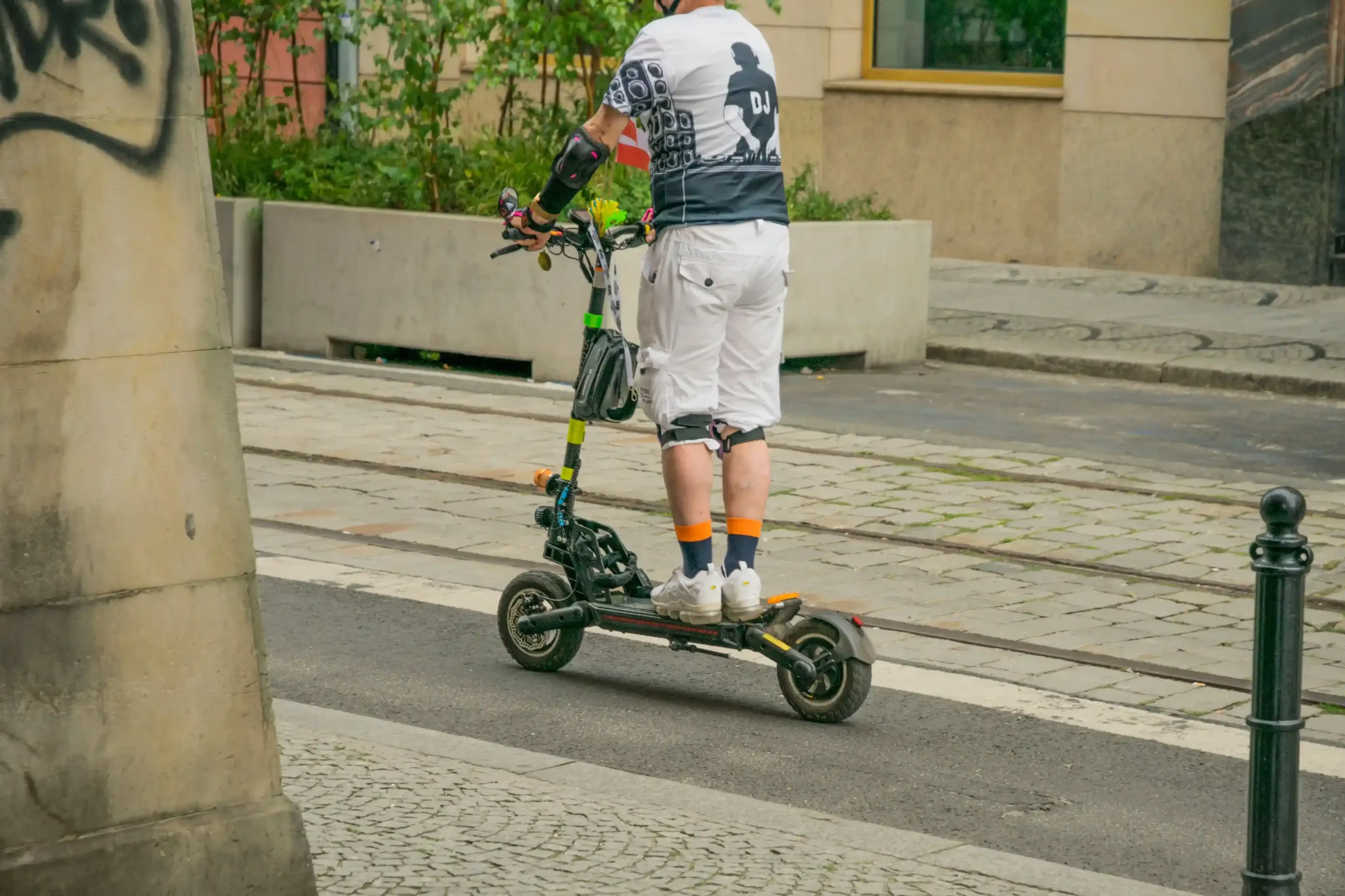 Fatbike ou trottinette électrique : Vue de dos d'un homme équipé de protections circulant en trottinette électrique robuste à double moteur sur une piste cyclable pavée en ville.