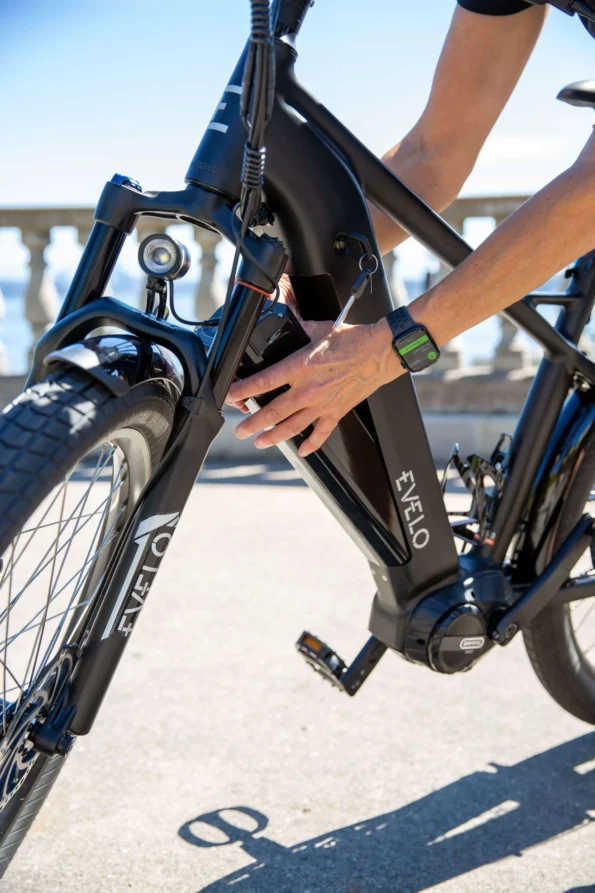 Gros plan d'une main manipulant la batterie noire amovible intégrée au cadre d'un vélo électrique EVELO pour illustrer comment entretenir la batterie de son vélo électrique au quotidien.